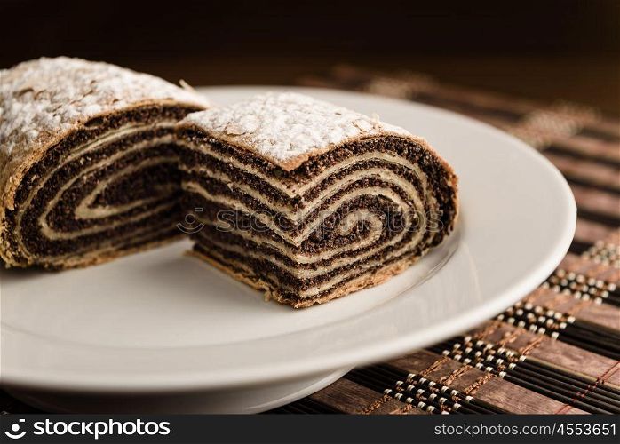 strudel with poppy seeds on a ceramic white plate on wooden background