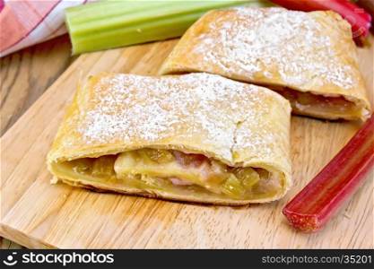 Strudel with rhubarb, napkin and stems on a wooden boards background
