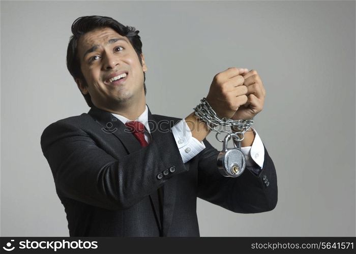 Struggling young businessman&rsquo;s hand tied in chain over gray background