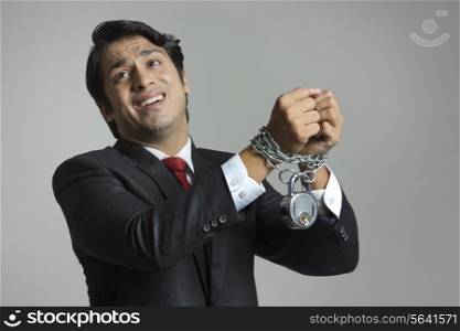 Struggling young businessman&rsquo;s hand tied in chain over gray background