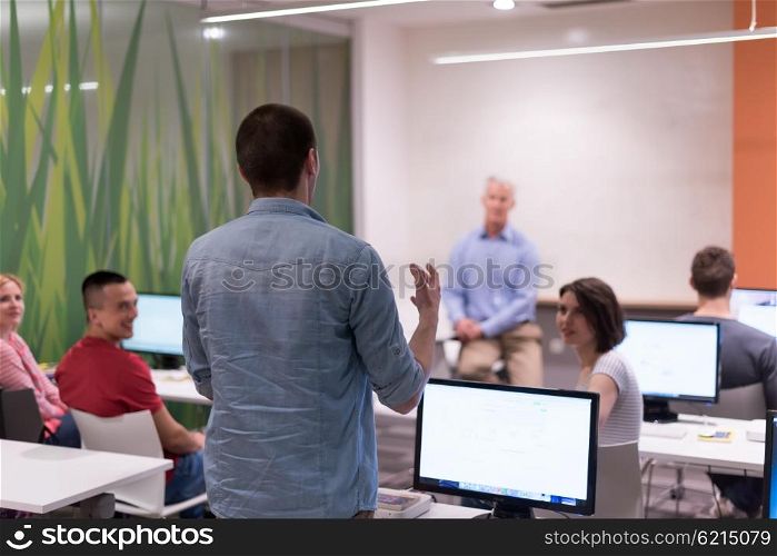 student answering a question in classroom, mature teacher and students in computer lab classroom