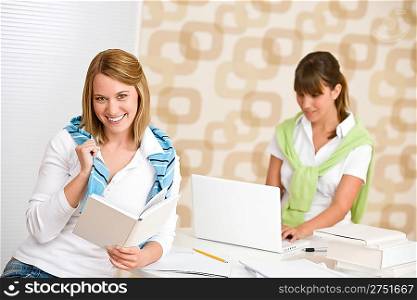 Student at home - two smiling woman with book and laptop study
