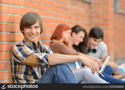 Student boy sitting by brick wall friends smiling in background