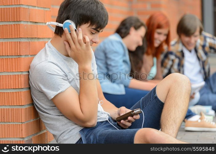 Student boy with headphones college friends sitting outside campus chatting