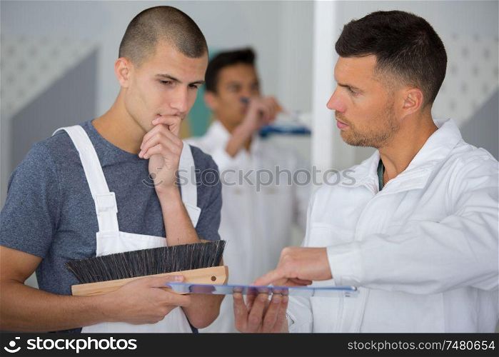 student decorator holding wallpapering brush talking to supervisor