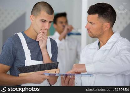 student decorator holding wallpapering brush talking to supervisor