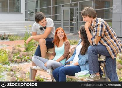 Student friends sitting on bench outside university campus laughing chatting