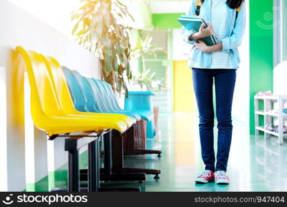 Student girl holding books and school bag standing over school background with copy space, education, back to school concept