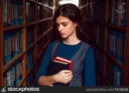 Student girl or woman with books between bookshelves in library.. Student girl or woman with books in library.