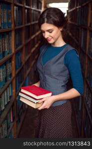 Student girl or woman with books between bookshelves in library.. Student girl or woman with books in library.