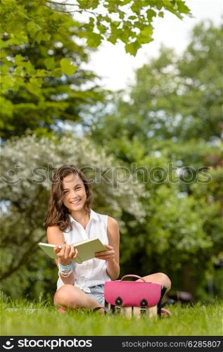 Student girl sitting on grass reading book pink school bag