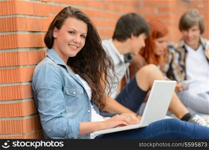 Student girl sitting with laptop outside campus friends in background