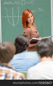 Student girl standing front of green chalkboard looking at classmates