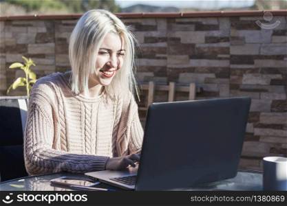 Student girl using laptop while sitting outdoors at home terrace.
