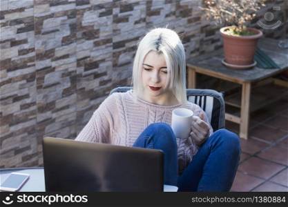 Student girl using laptop while sitting outdoors at home terrace.