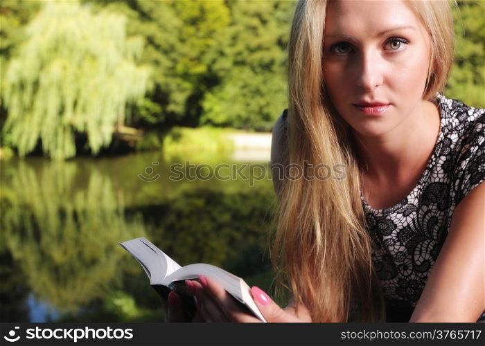 Student girl with open book, young woman lies and reading relaxing on green background of city park.