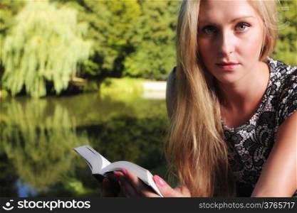 Student girl with open book, young woman lies and reading relaxing on green background of city park.