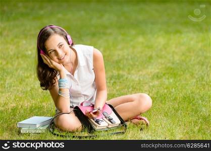 Student girl with pink headphones sitting on grass summer