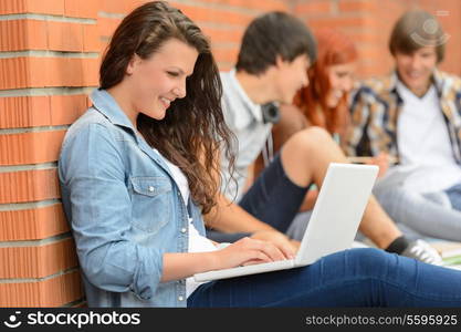 Student girl working on laptop outside college friends in background