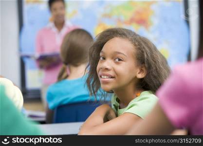 Student in class looking at camera with teacher in background (selective focus)
