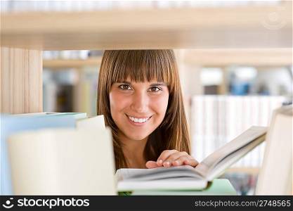 Student in library - cheerful woman hold book stand by bookshelf