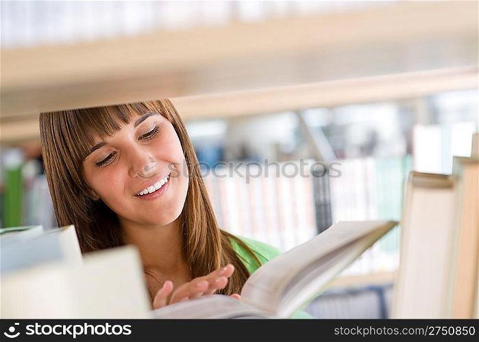 Student in library - cheerful woman read book from bookshelf