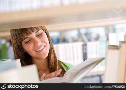 Student in library - cheerful woman read book from bookshelf