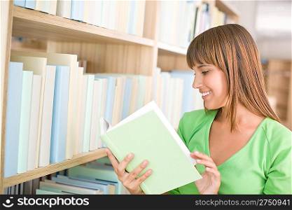 Student in library - happy woman read book from bookshelf
