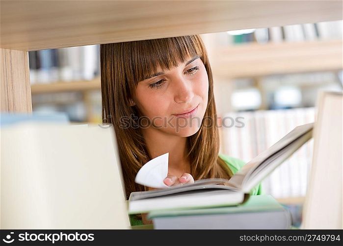Student in library - happy woman read book stand at bookshelf