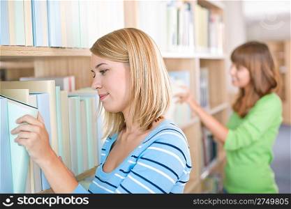 Student in library - two woman search for book in bookshelf