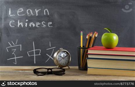 Student learning Chinese with books, pencils, clock, reading glasses and an apple in front of chalkboard with Mandarin text.