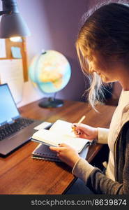 Student learning remotely from home. Young woman having classes online, making notes, reading and learning sitting at desk at home during quarantine