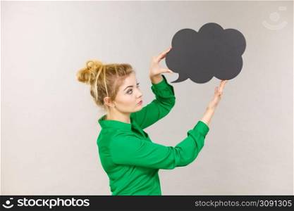 Student looking business woman wearing green shirt holding black thinking bubble on grey background.. Woman holding black thinking bubble