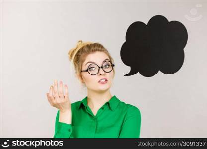Student looking business woman wearing green shirt talking, black thinking bubble on grey background.. Woman holding black thinking bubble