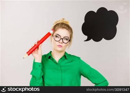 Student looking woman wearing nerdy eyeglasses holding big oversized pencil thinking about something, black speech bubble next to her. Woman holding big oversized pencil thinking