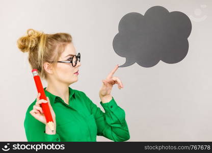 Student looking woman wearing nerdy eyeglasses holding big oversized pencil thinking about something, black speech bubble next to her. Woman holding big oversized pencil thinking