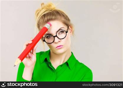 Student looking woman wearing nerdy eyeglasses holding big oversized pencil thinking about something.. Woman holding big oversized pencil thinking about something
