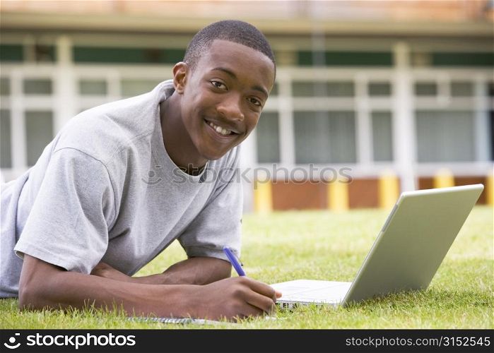 Student lying outdoors on lawn with laptop