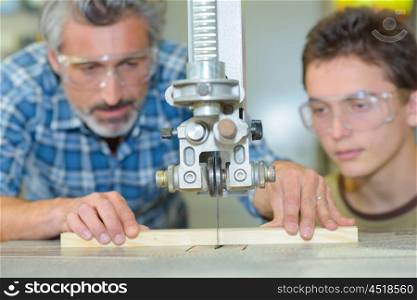 Student observing teacher sawing wood