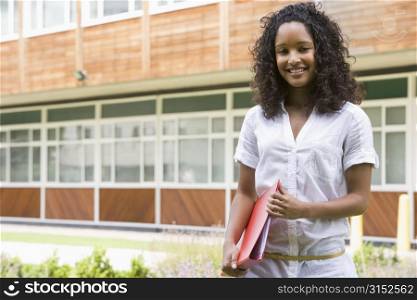 Student standing outdoors smiling and holding binder