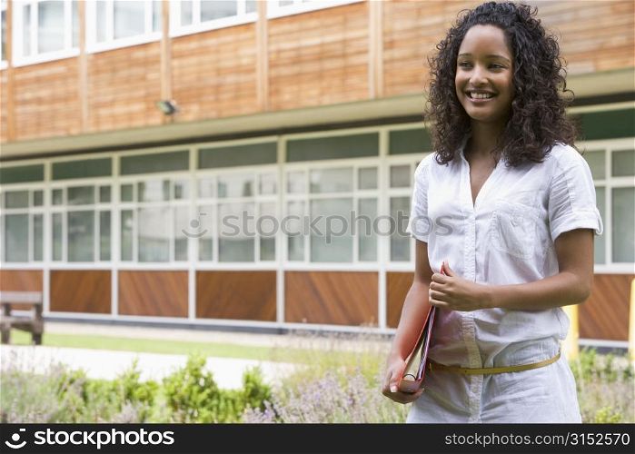Student standing outdoors smiling and holding binder
