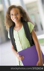 Student standing outside school holding binder and smiling (selective focus)