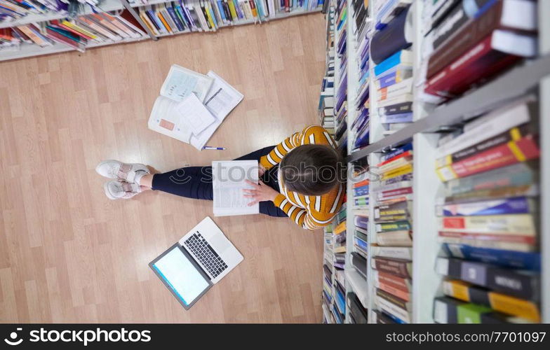 student taking notes from a book at library. Young woman sittingin in school library and working with laptop