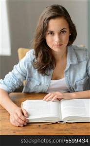 Student teenage girl reading book at home sitting behind wooden table