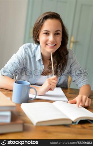 Student teenage girl studying at home sitting behind table smiling