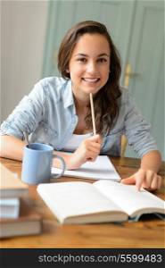 Student teenage girl studying at home sitting behind table smiling