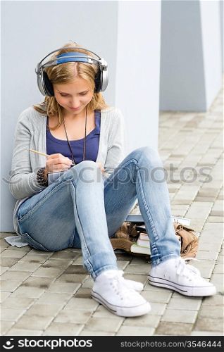 Student teenager make school notes and listen to music
