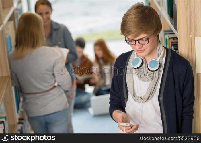 Student with headphones using mobilephone with friends in library