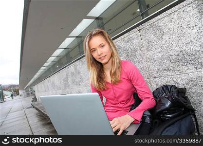 Student with laptop computer sitting outside school building