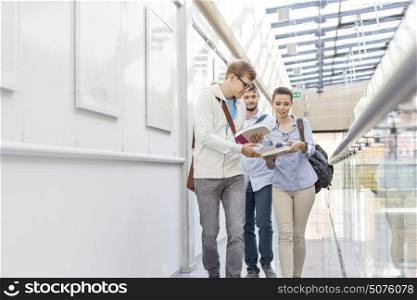 Students exchanging books while walking in corridor at college